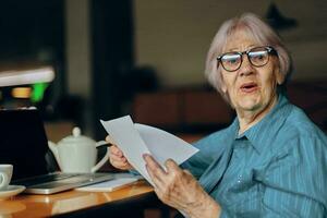 Portrait of an elderly woman with glasses sits at a table in front of a laptop Lifestyle unaltered photo