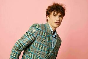 Young curly-haired man gesturing with his hands emotions checkered jacket pink background unaltered photo