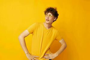 Young curly-haired man wearing stylish glasses yellow t-shirt posing isolated background unaltered photo