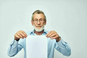 antiguo hombre en un azul camisa y lentes un blanco sábana de papel ligero antecedentes foto