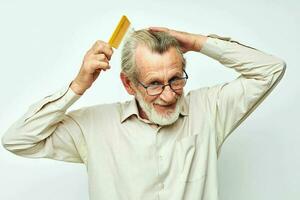 Elderly man combing hair with yellow comb in studio photo