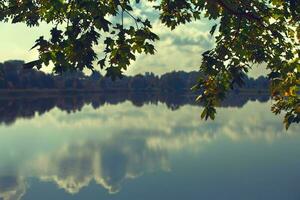 Beautiful landscape lake with clouds and autumn leaves reflected in it. Forest reservoir. photo