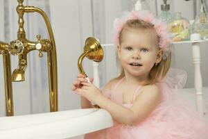 pequeño gracioso niña en un inteligente rosado vestir en el baño. foto