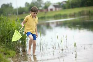 A little boy with a fishing net walks near the lake and looks at the water. photo