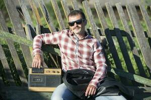 un gracioso hombre con un casete grabadora se sienta por un de madera cerca. foto