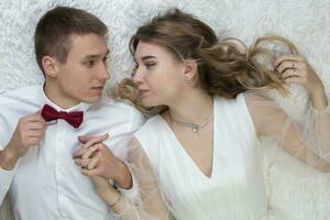 Beautiful loving couple bride and groom lie on the bed and look at each other. photo