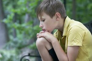 The sad little boy put his head on his knee. The child is bored. photo