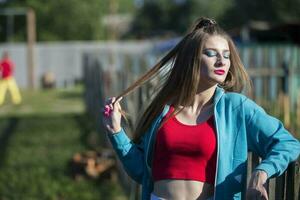 A beautiful girl in bright clothes stands near a wooden fence. Woman in the style of the 90s. photo