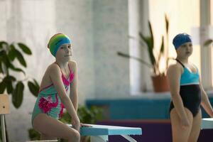muchachas en un traje de baño y un nadando gorra con lentes en el Deportes piscina. foto