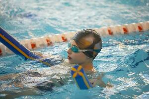 Boy in a swimming cap and swimming goggles in the pool. The child is engaged in the swimming section. photo