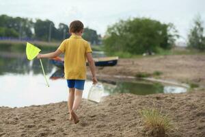 A little boy with a fishing net walks along the shore of the lake. photo