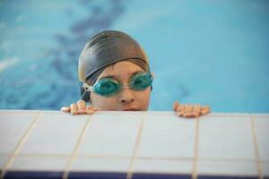 Boy in a swimming cap and swimming goggles in the pool. The child is engaged in the swimming section. photo