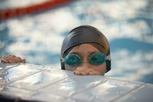 Boy in a swimming cap and swimming goggles in the pool. The child is engaged in the swimming section. photo