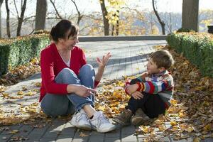 Mom and little one are sitting and talking cheerfully in the autumn park. photo