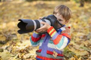 A little boy is holding a camera with a large lens. Young photographer. photo