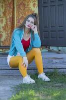 A beautiful girl in bright clothes sits on the porch of a village house. Woman in the style of the 90s. photo