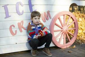 A little boy sits in the park near the wall with the inscription Ice Cream. The child went out for a walk. photo