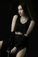 A beautiful young girl with long hair in black short clothes on a dark background. photo