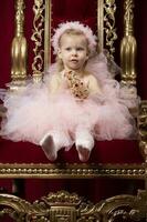 A little funny girl in a chic pink dress sits in a luxurious armchair. photo