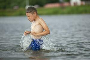 A little boy runs into a cold river. The child swims in the lake in summer. photo