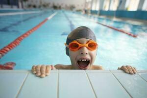 chico en un nadando gorra y nadando gafas de protección en el piscina. el niño es comprometido en el nadando sección. foto