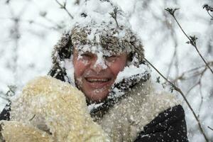 A frozen man covered in snow in winter smiles and looks at the camera. The first snow fell. A man in a fur hat in cold weather. photo