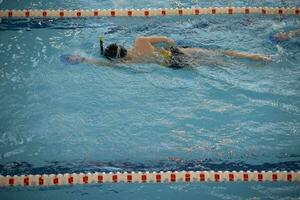 chico en un nadando gorra y nadando gafas de protección en el piscina. el niño es comprometido en el nadando sección. foto