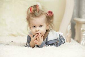 A cute little girl in curlers lies on the bed and looks at the camera. photo