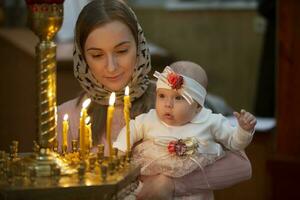 madre y niño en un Iglesia por luz de una vela. mujer con un bebé en el templo. foto