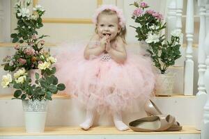 dos años de edad niño. un hermosa pequeño niña en un elegante rosado vestir y alto tacón Zapatos se sienta en el porche. foto