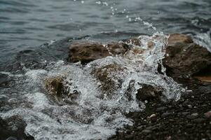 Image of the sea surf. A large wave is beating against a stone on the seashore. Ocean surf among the rocks. Background of the tide. Sea foam photo