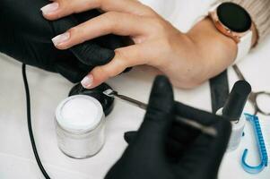 A manicure master gives a manicure to a girl in the salon. Close-up. The manicure master strengthens the client's nail with powder. photo