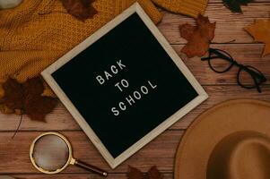 otoño accesorios, plano sombrero, suéter, hojas arce, madera letra tablero con texto espalda a escuela, lentes. foto