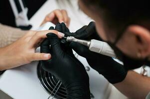 Hardware manicure. Close-up of a manicure master filing gel polish with a nail grinder with a cutter. photo