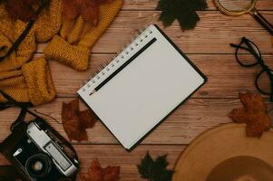 Autumn accessories, flatlay. Hat, sweater, leaves maple, glasses, notepad, retro camera on wooden background. Copying space photo