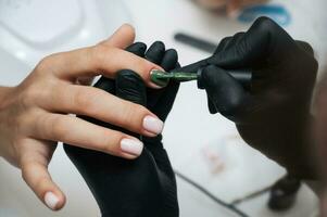 Manicure service. Close-up. Applying green varnish . The manicurist paints her nails with a transparent gel polish. Well-groomed nails. Professional salon hand care. photo