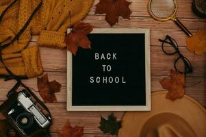 Autumn accessories, flatlay. Hat, sweater, leaves maple,wooden letter board with text Back to school, glasses, retro camera. photo