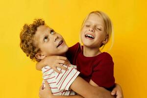 alegre niños en pie lado por lado posando infancia emociones amarillo antecedentes foto