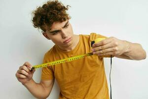 Attractive man measuring tape measure in yellow t-shirt light background photo