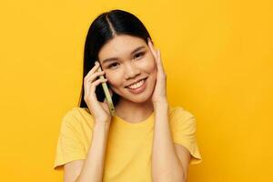 encantador joven asiático mujer hablando en el teléfono posando tecnología amarillo antecedentes inalterado foto