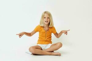 pequeño niña con rubio pelo gesticulando con su manos mientras sentado en el piso foto