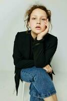 hermosa mujer sentado en un silla en un negro chaqueta Moda posando ligero antecedentes inalterado foto