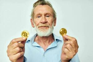 Senior grey-haired man in a blue shirt bitcoins on the face isolated background photo