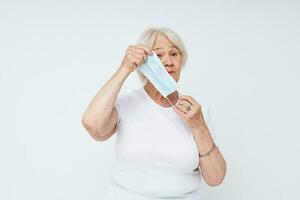 elderly woman in casual t-shirt and medical mask light background photo