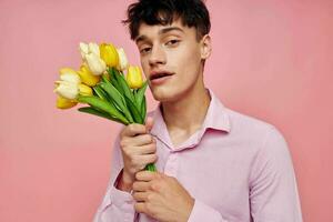 retrato de un joven hombre en un rosado camisa con un ramo de flores de flores gesticulando con su manos estilo de vida inalterado foto