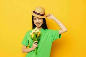 Charming young Asian woman green t-shirt a bouquet of yellow flowers in a hat isolated background unaltered photo