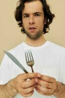 atractivo hombre en un blanco camiseta con cuchillo con tenedor aislado antecedentes foto