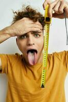 handsome young man measuring tape measure in yellow t-shirt light background photo