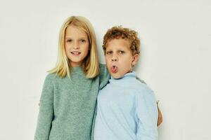 Photo of two children in multi-colored sweaters posing for fun light background