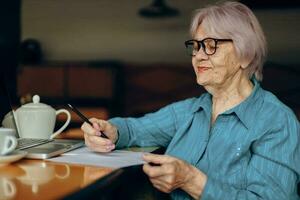 mayor mujer con lentes se sienta a un mesa en frente de un ordenador portátil persona de libre dedicación trabajos inalterado foto